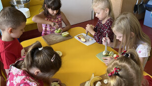 dzieci siedzą przy stolikach robią sałatkę
